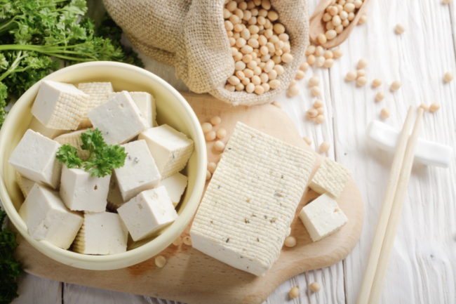 Soy Bean curd tofu in clay bowl and in hemp sack on white wooden kitchen table. Non-dairy alternative substitute for cheese